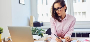 Busy young woman working in office with documents and laptop.