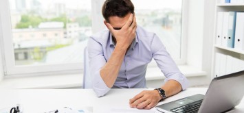 Businessman with laptop computer and papers stressed working in office.