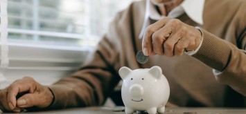 Old man putting money in the piggy bank