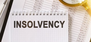 On the table are financial reports, a pen, a magnifying glass and a notebook with the inscription - INSOLVENCY.