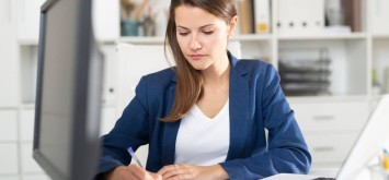 Focused young business woman working alone with laptop and documents in office.